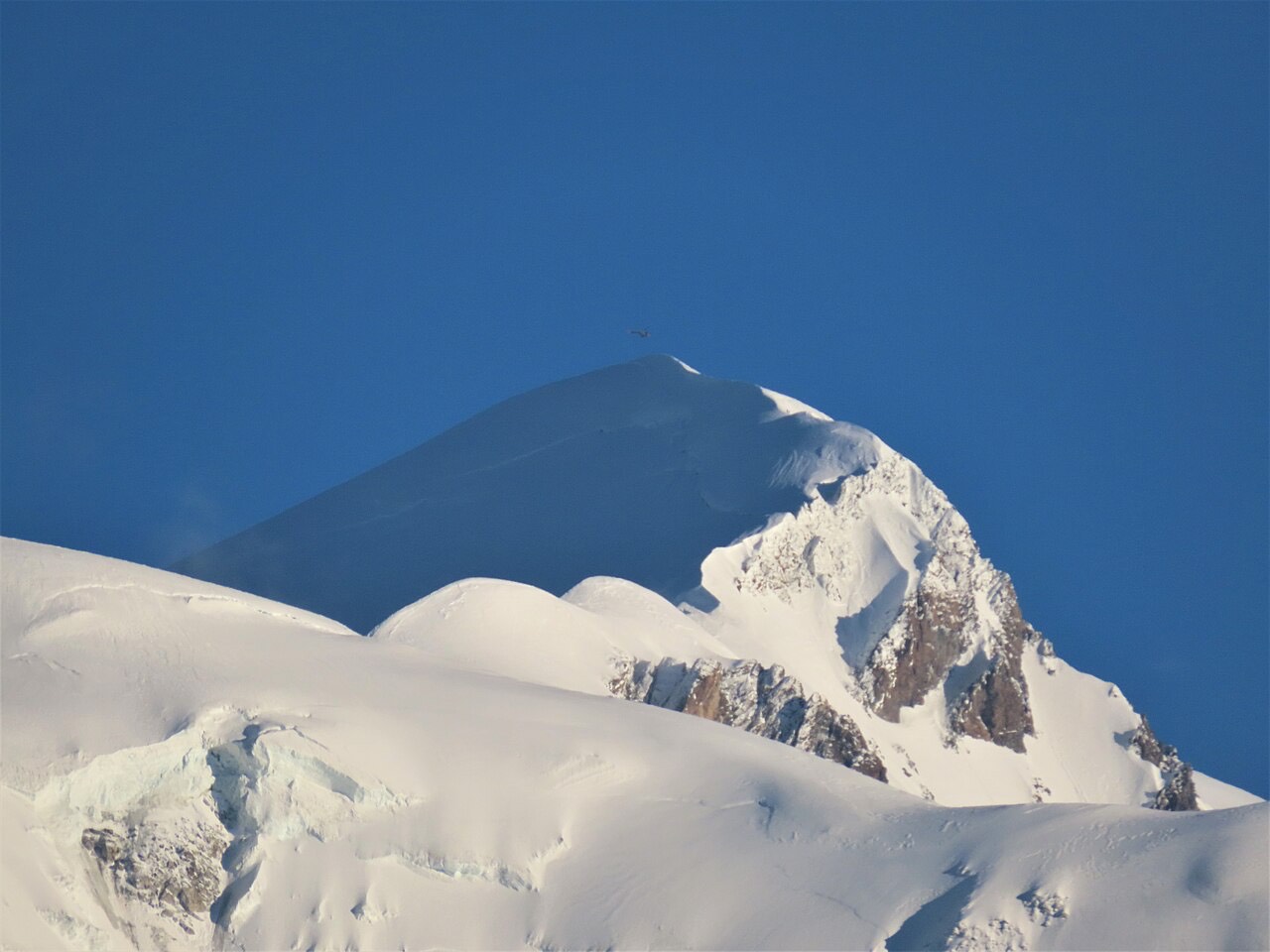 The snow-covered summit dome of Mont Blanc rising above a ridge of glaciers.